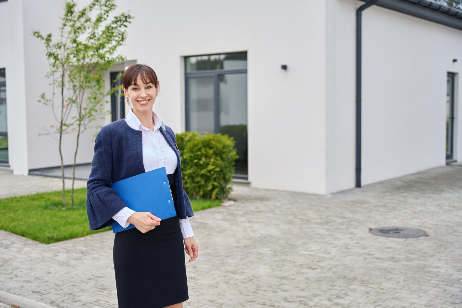 Lady has a blue folder with documents in her hands, she is standing in the courtyard of a country house